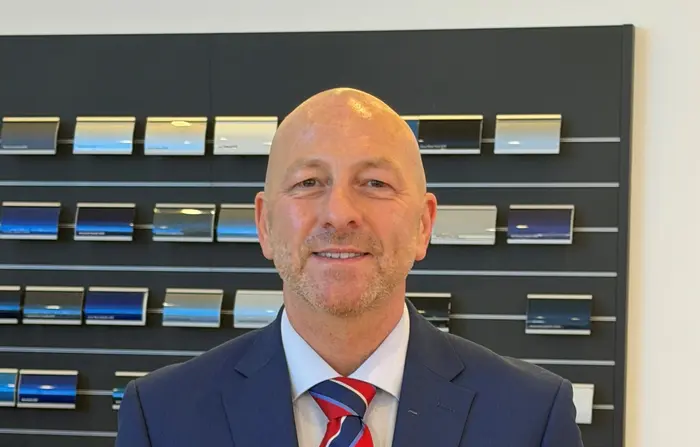 Ian Williams standing beside the Athenea Automotive Group logo