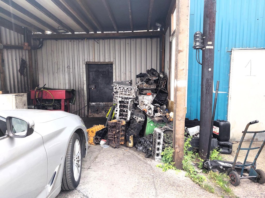 Piles of dismantled vehicle parts and components visible at the chop shop site